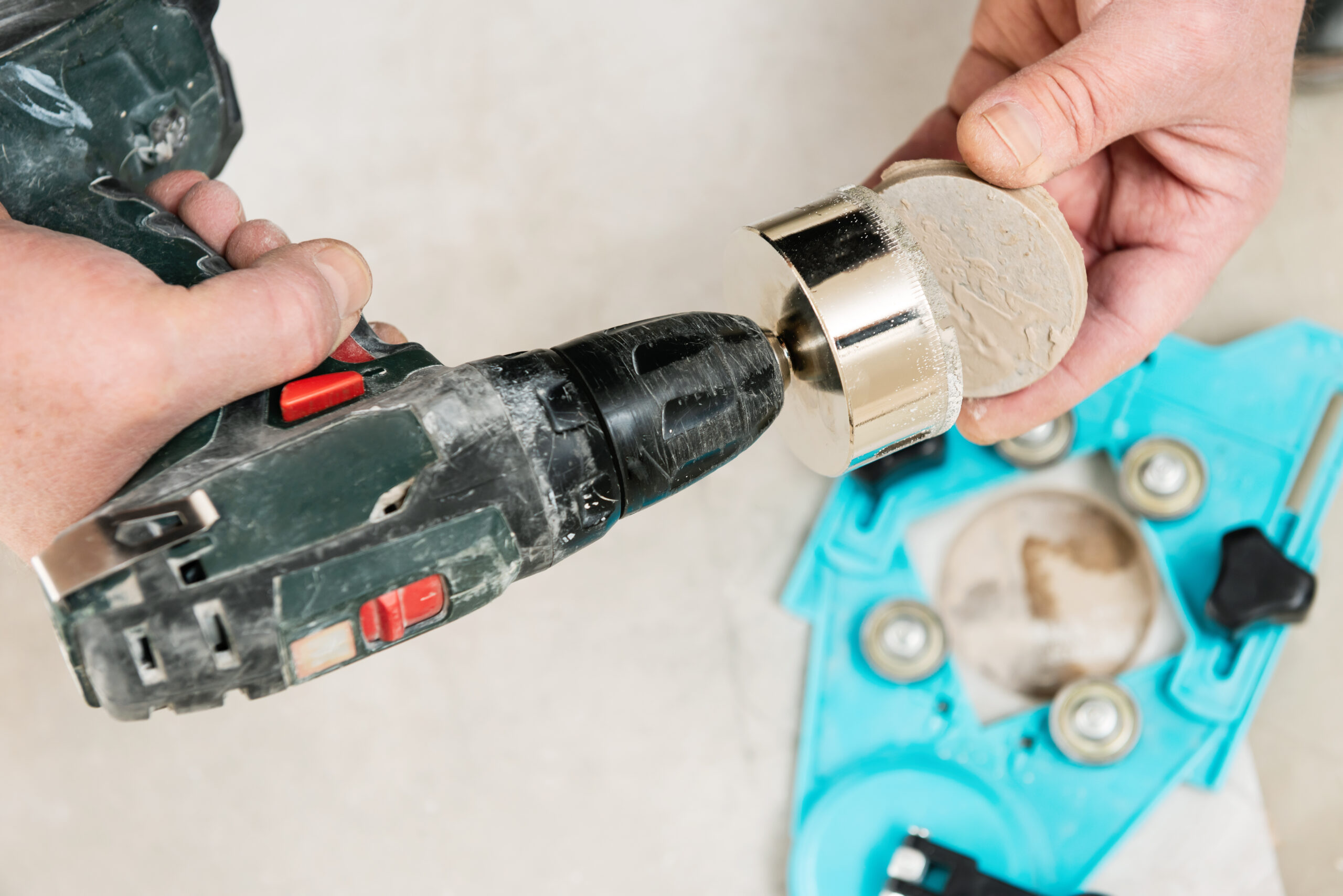 A tiler is using a diamond crown to drill holes in the ceramic tile.